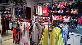 На этом фото мы видим по центру стойку для магазина одежды двойную и плечики с товаром. По периметру слева направо: торсы манекены женские и далее стойку для одежды настенную укомплектованную рейками и перемычками на которые закреплены вешала.