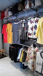 Вид с другого ракурса. Вешала для одежды волнообразные вверху, снизу дуга хромированная. На вешалах одежды лицом, на дугах боком.