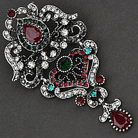 Брошка металева на сріблястій основі класична з рубіновими та смарагдовими кристалами розмір 80х40 мм
