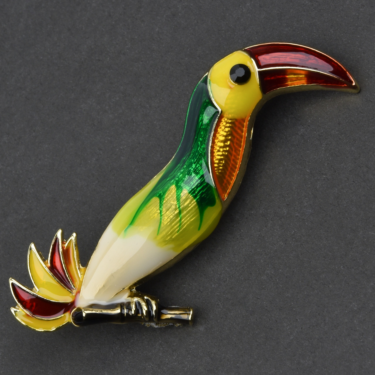 Брошка металева на золотистій основі тукан на гілочці з камінчиком покрита кольоровою емаллю розмір 40х45 мм