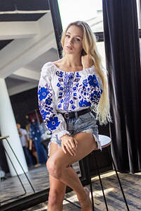 Жіноча біла вишиванка з синьою вишивкою хрестиком та квітковим орнаментом на рукавах