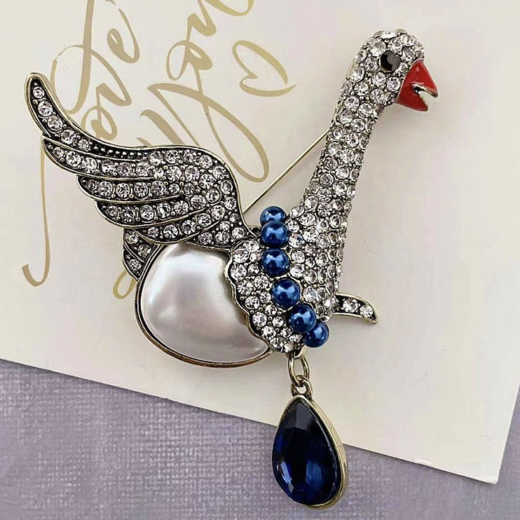 Брошка металева на золотистій основі гусак із білими стразами із синіми намистинами та кристалом розмір 85х65 мм