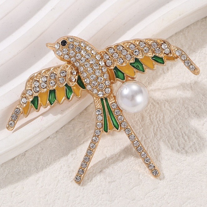 Брошка металева на золотистій основі ластівка з білими стразами покрита кольоровою емаллю розмір 60х55 мм