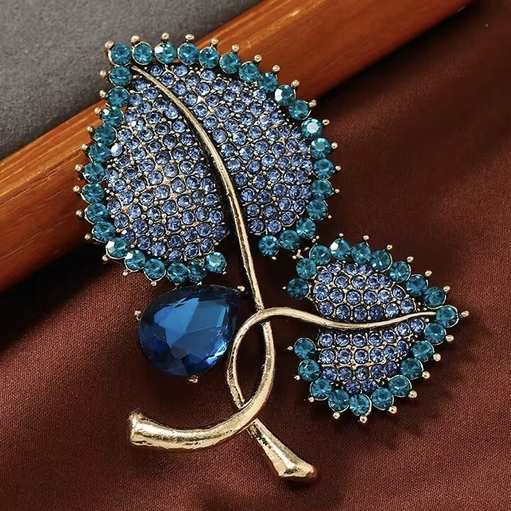 Брошка на золотистій основі листочки з блакитними та бірюзовими камінчиками розмір виробу 70х55 мм