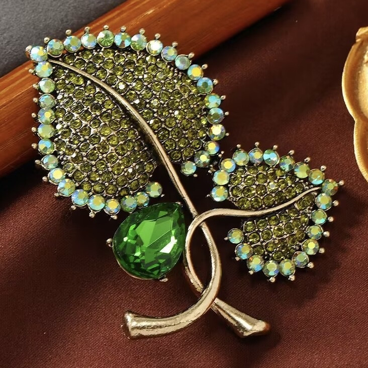 Брошка на золотистій основі листочки із зеленими кристалами, що переливаються, розмір виробу 70х55 мм