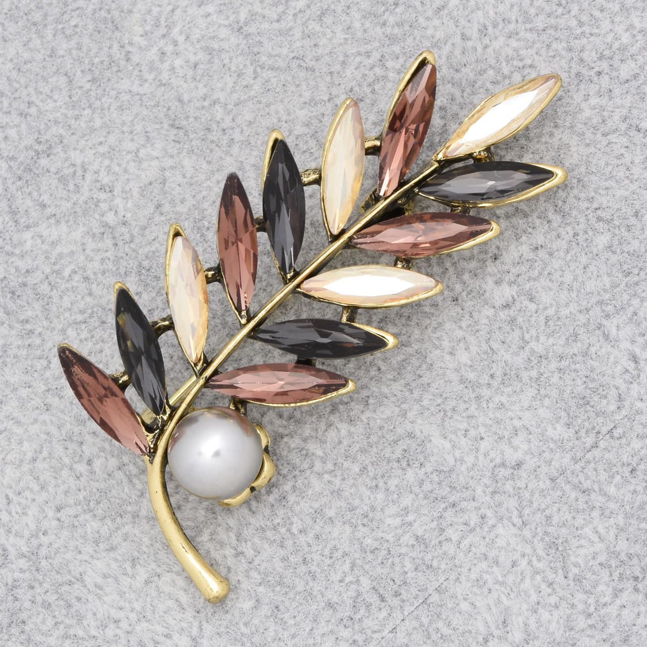 Брошка на золотистій основі листочок із різнобарвними кристалами та білою намистиною розмір виробу 65х25 мм