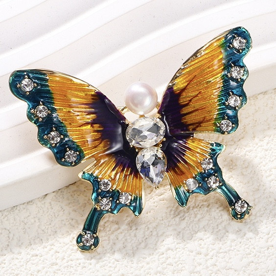 Брошка на золотистій основі метелик із білими стразами та намистиною покрита кольоровою емаллю розмір 50х40 мм