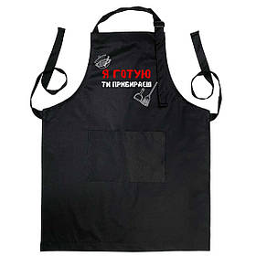 Фартух чорного кольору з лямкою, що регулюється і кишенею "Я готую, ти прибираєш"