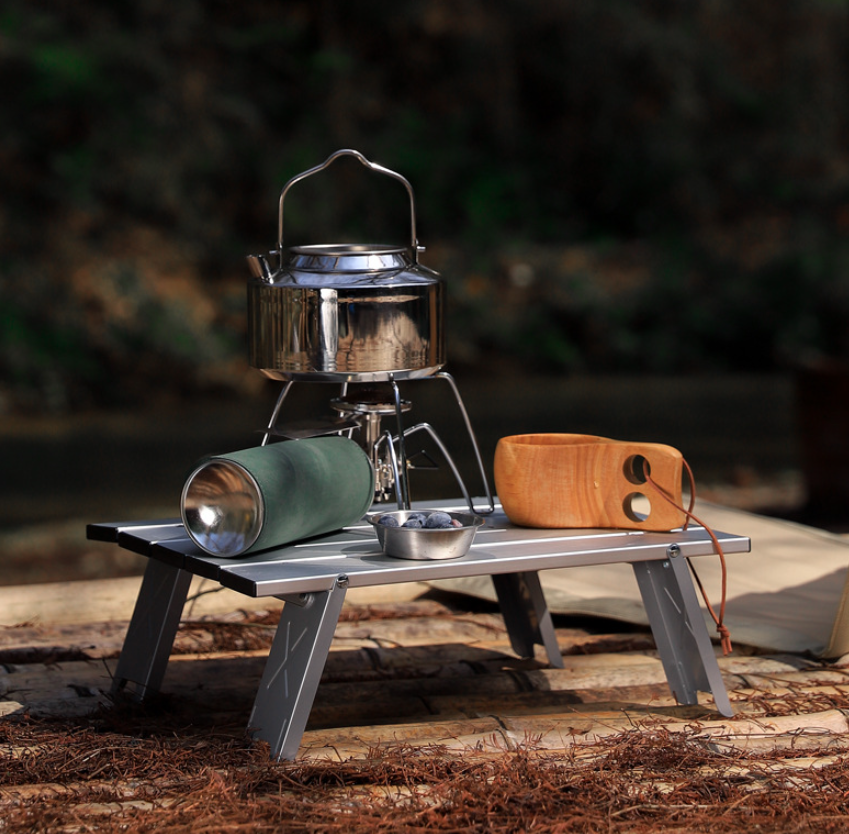 Міцний алюмінієвий стіл для газової плити, на якому стоїть похідна пальник із чайником, що кипить.