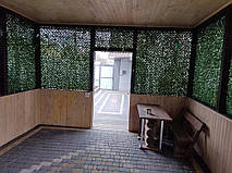 Інтер’єр альтанки з декоративною зеленою сіткою по стінах. Сітка створює захищений простір, не перекриваючи доступ світла та повітря.